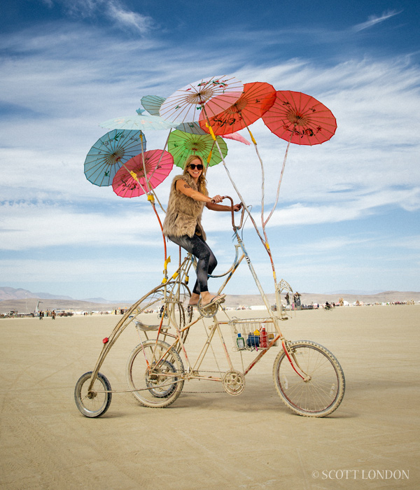 A woman rides a modified bike with multicolored parasols at Burning Man 2016. (Photo by Scott London)