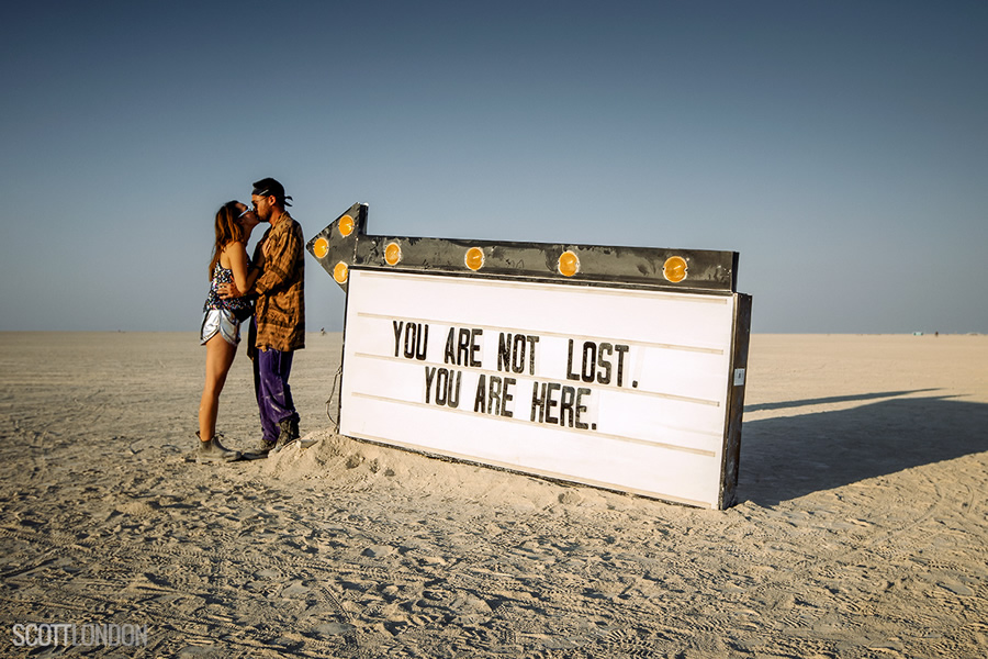 A couple kiss next to a sign that reads 'You Are Not Lost - You Are Here' at Burning Man 2017. (Photo by Scott London)